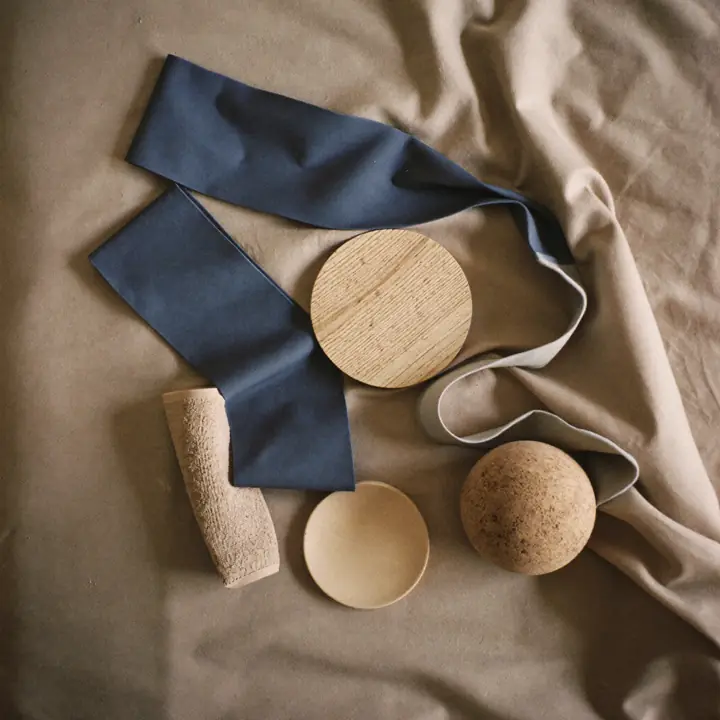 Three resistance bands loosely coiled in slate blue, sand and grey on washed linen, beside a small round wooden balance board, a cork ball and a folded towel