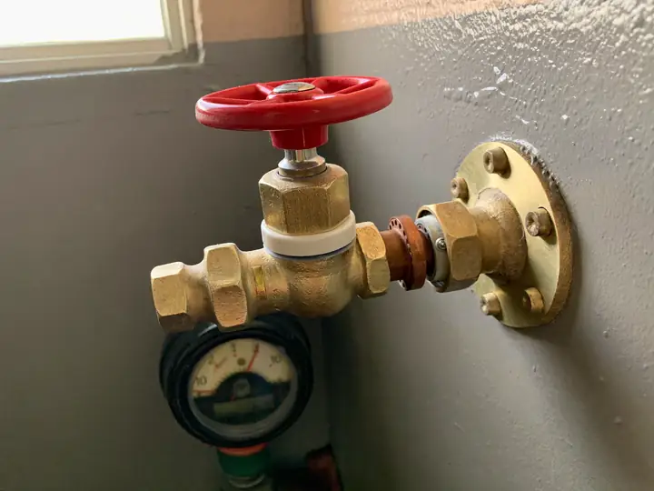 A brass main water shutoff valve with a red handle on a copper pipe